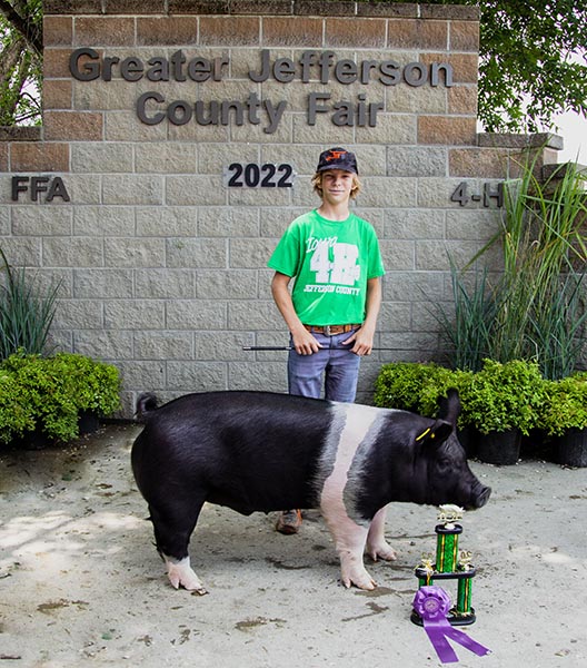 Rider Robertson Champion Carcass Pig A boy standing next to a black and white pig.