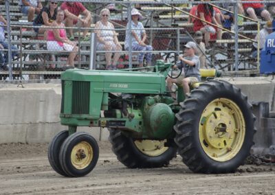 A green tractor with yellow wheels driving down the road.
